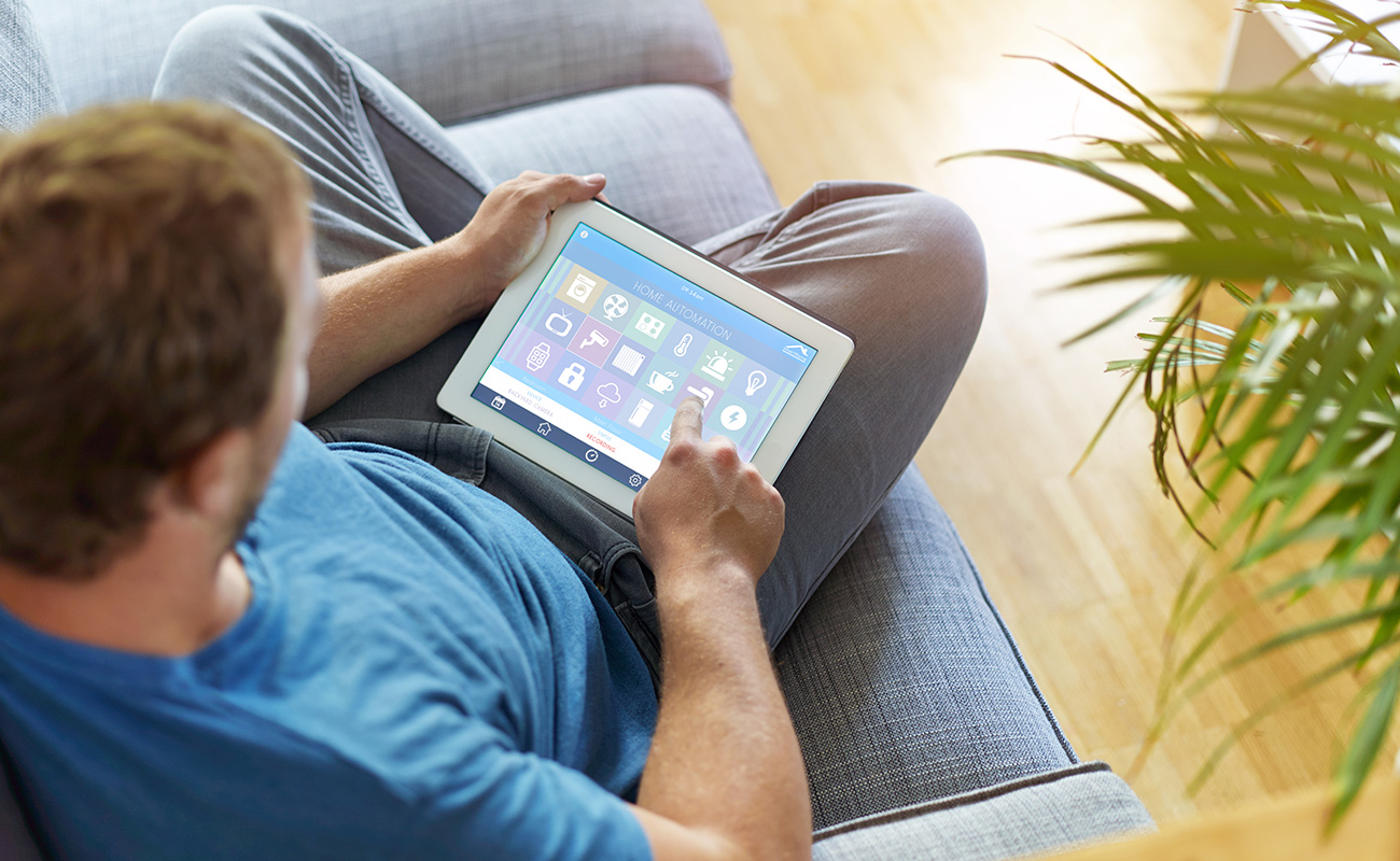Man sitting on couch controlling tv through a tablet