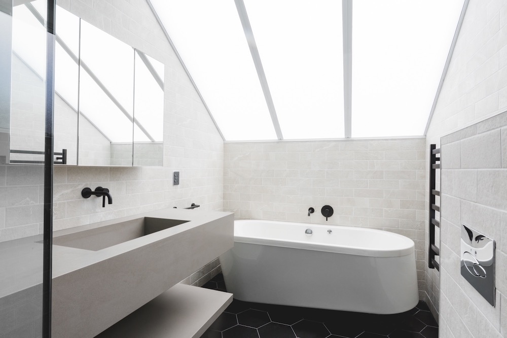 Modern bathroom with a skylight, featuring a freestanding bathtub, floating vanity with a large mirror and black fixtures
